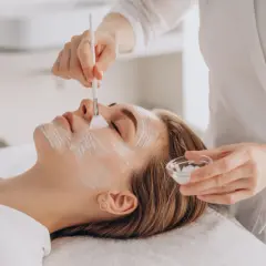 Kwasowy peeling enzymatyczny delikatnie pieści skórę, nie powinien piec. Kosmetyczka nakłada maskę na twarz klientki.