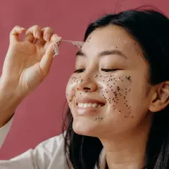 Kobieta z brokatem na twarzy zdejmuje maskę. To pokazuje, co to peeling - oczyszczanie skóry.